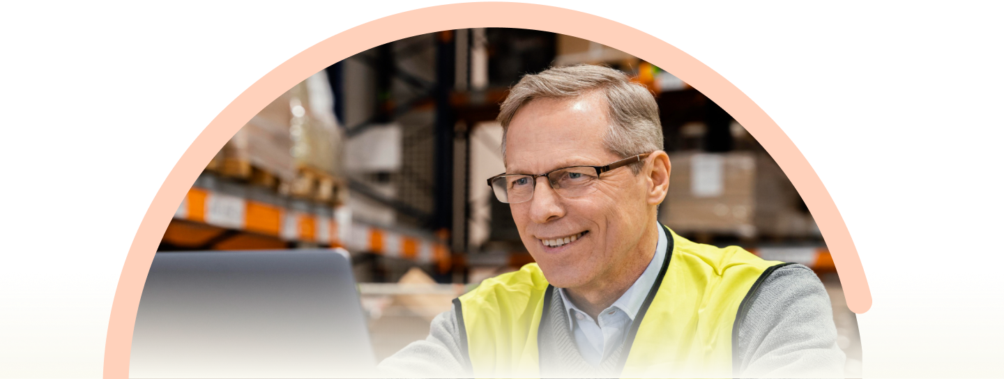 Smiling warehouse manager in yellow safety vest and glasses standing in modern distribution facility